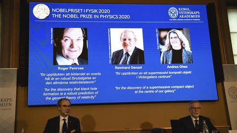 Die drei Preisträger auf dem Bildschirm von links, Roger Penrose, Reinhard Genzel und Andrea Ghez, haben den diesjährigen Nobelpreis in Physik für die Entdeckungen schwarzer Löcher erhalten. (Foto: picture-alliance / Reportdienste, picture alliance/Fredrik Sandberg/TT News Agency/dpa)