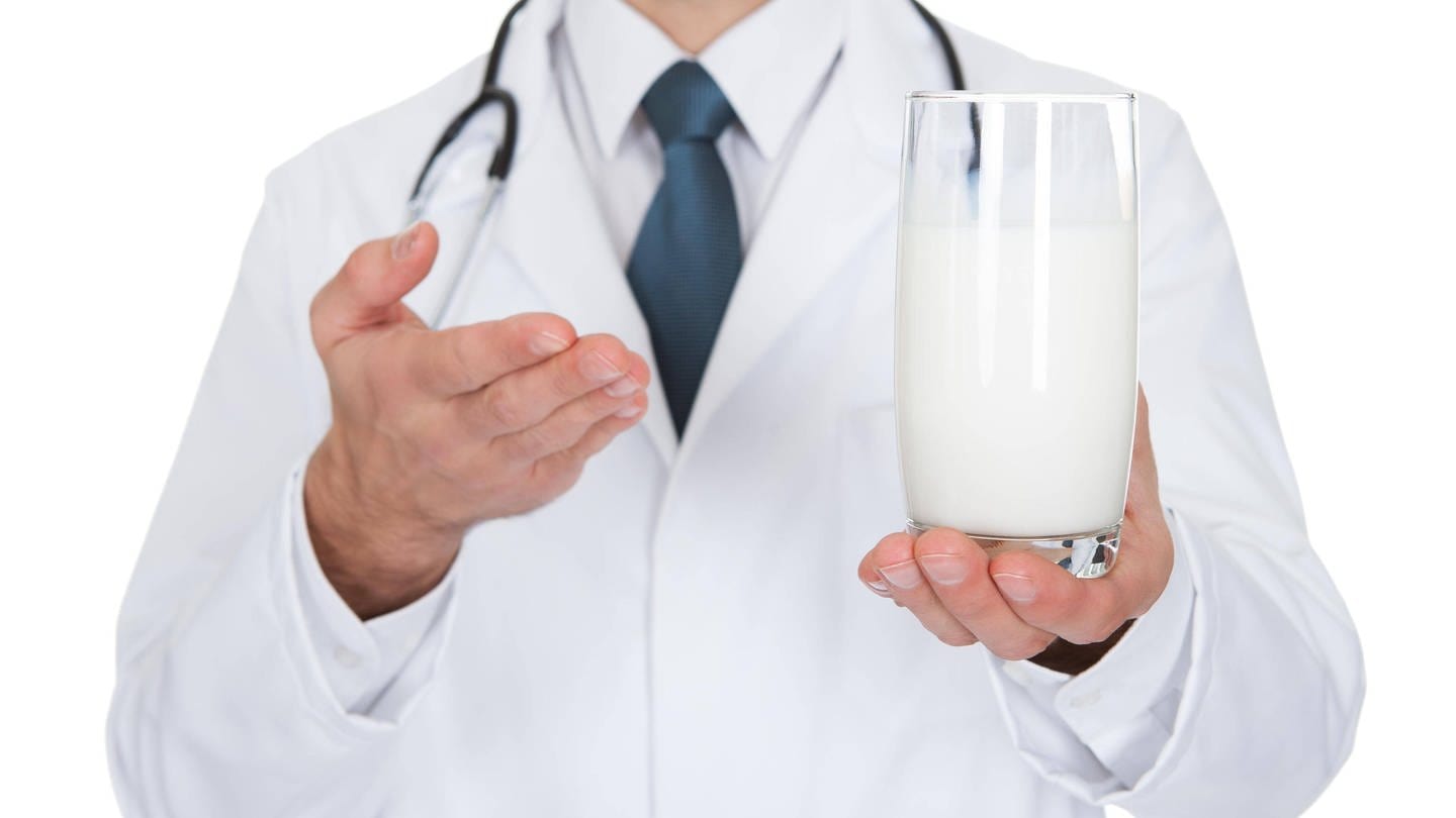 Arzt zeigt auf ein Glas Milch: Stimmt es, dass man Antibiotika nicht mit Milch einnehmen sollte? (Foto: IMAGO, IMAGO / Panthermedia)