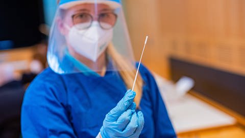 Medizinische Mitarbeiterin in Corona-Schutzkleidung hält Nasenabstrich in der Hand. (Foto: IMAGO, IMAGO / KS-Images.de)