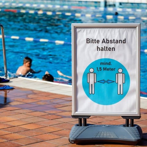 Ein Schild mit der Aufschrift "Bitte Abstand halten" steht vor dem Schwimmbecken eines Freibads. (Foto: IMAGO, IMAGO / Rupert Oberhäuser)