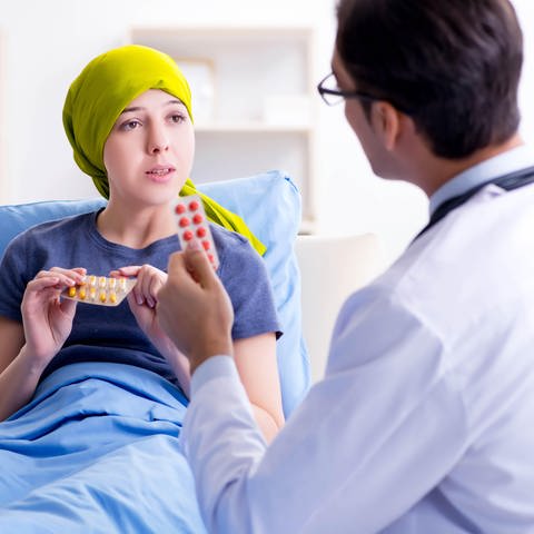 Frau mit Glatze unter ihrem gelben Kopftuch redet mit Arzt über ihre Chemotherapie: Eine Chemotherapie hat oft Haarausfall als Nebenwirkung (Foto: dpa Bildfunk, picture alliance / Zoonar)