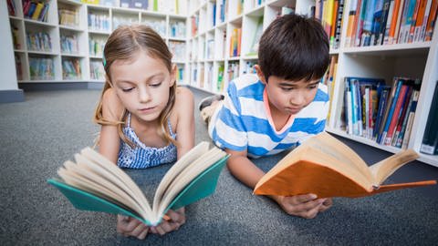 Zwei Kinder liegen auf dem Boden und lesen Bücher: Die Intelligenz von Kindern sagt den späteren beruflichen Status besser vorher als es der berufliche Status der Eltern tut