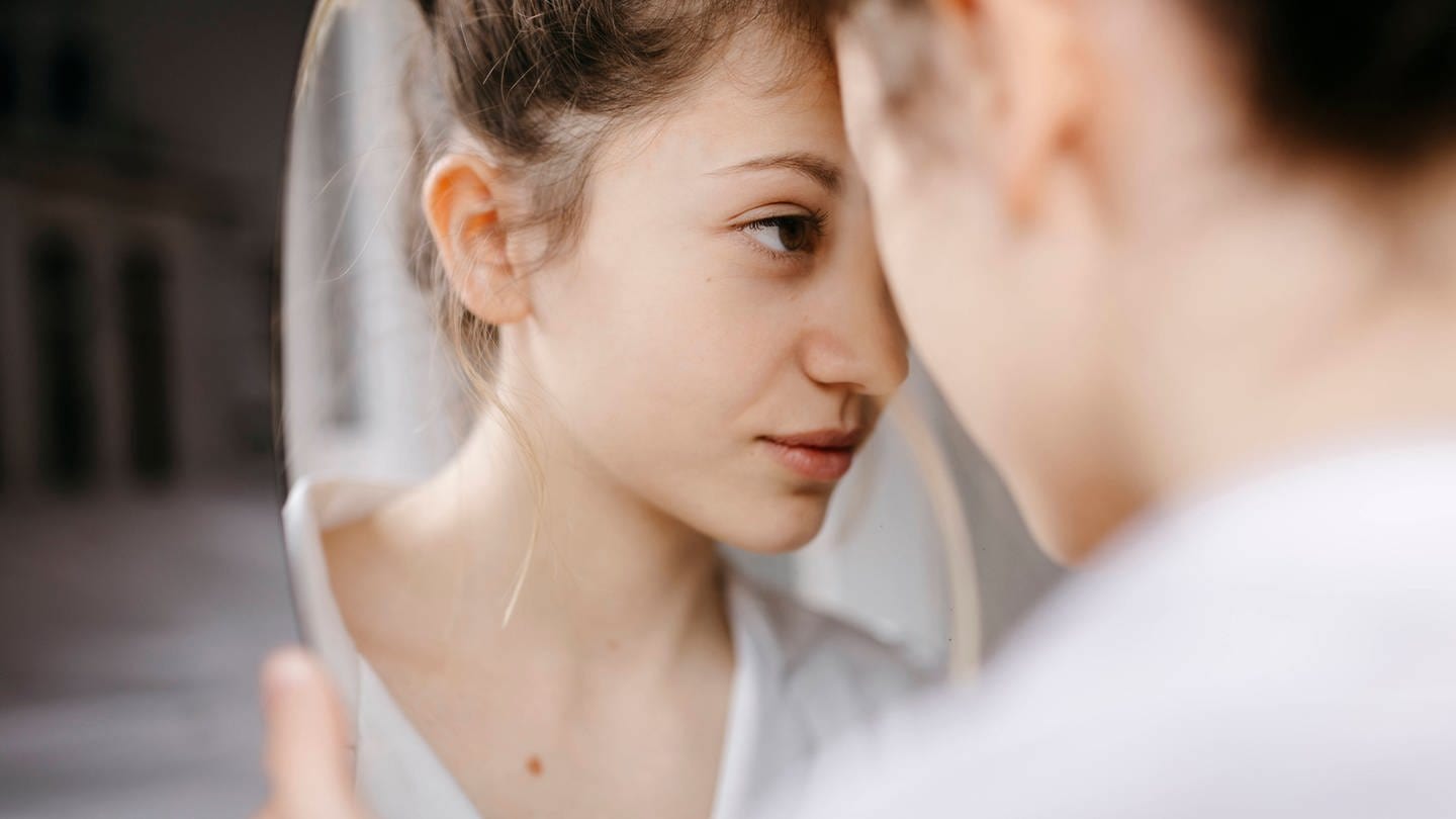 Eine junge Person schaut ganz nah in einen Spiegel (Foto: IMAGO, Tania Cervian via www.imago-images.de)
