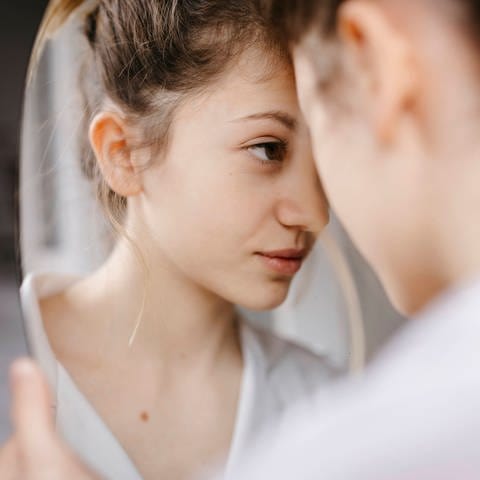 Eine junge Person schaut ganz nah in einen Spiegel (Foto: IMAGO, Tania Cervian via www.imago-images.de)