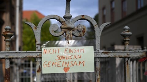 Ein Tor mit einem selbst gemalten Schild mit der Aufschrift: "Nicht einsam sondern gemeinsam" (Foto: IMAGO, fossiphoto via www.imago-images.de)