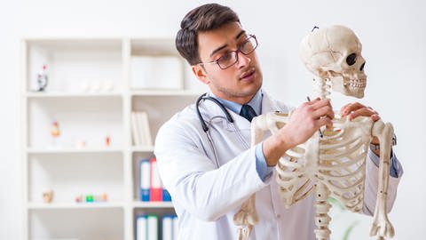 Mann in Arztkleidung verdreht den Kopf eines Skelettes (Foto: IMAGO, Elnur via www.imago-images.de)