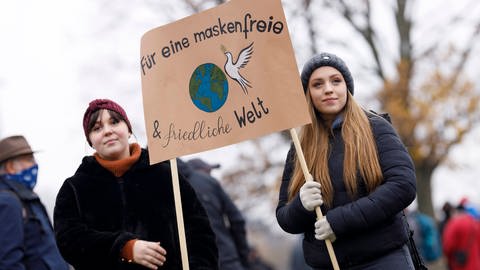 Demonstrantinnen auf einer Düsseldorfer Querdenken-Demo gegen das Tragen von Masken im Dezember 2020, sie halten ein Plakat hoch mit der Aufschrift: "Für eine maskenfreie und friedliche Welt" (Foto: IMAGO, Christoph Hardt via www.imago-images.de)