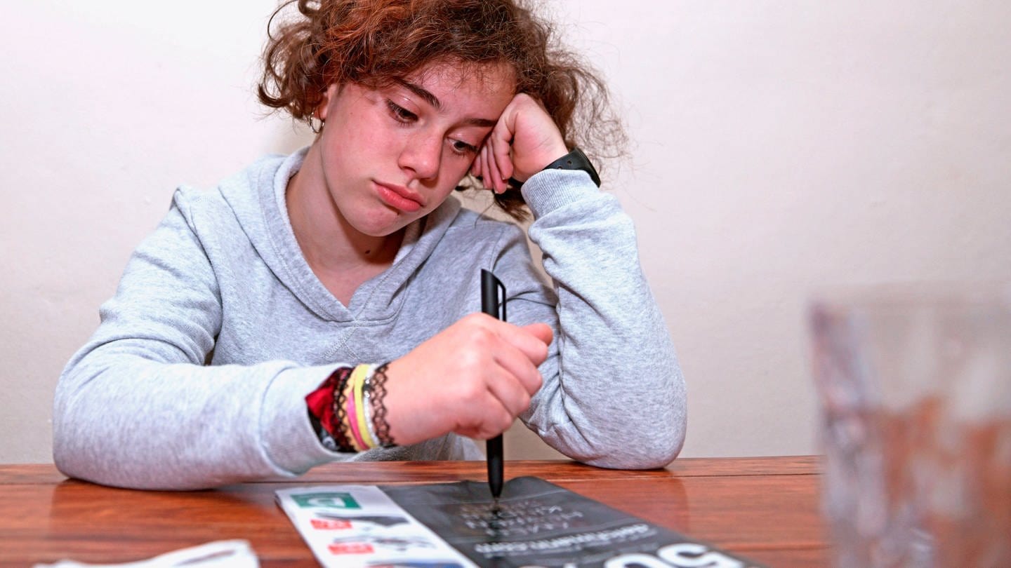 Ein Schulkind muss wegen der Corona-Pandemie Unterricht von Zuhause aus machen, es schaut traurig und gelangweilt (Foto: IMAGO, imago images/MiS)