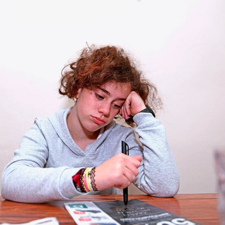 Ein Schulkind muss wegen der Corona-Pandemie Unterricht von Zuhause aus machen, es schaut traurig und gelangweilt (Foto: IMAGO, imago images/MiS)
