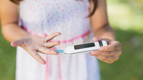Ein Mädchen prüft an ihrem rechten Ringfinger mit einem Glukometer ihren Blutzuckerspiegel. (Foto: IMAGO, IMAGO / YAY Images)