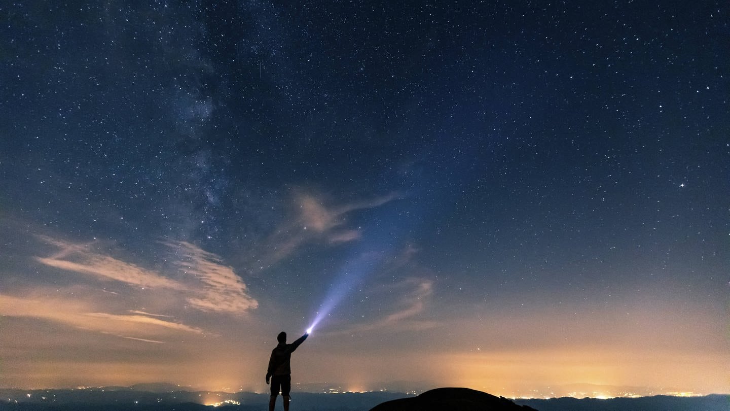 Ein Mensch leuchtet mit einer Taschenlampe gen Sternenhimmel