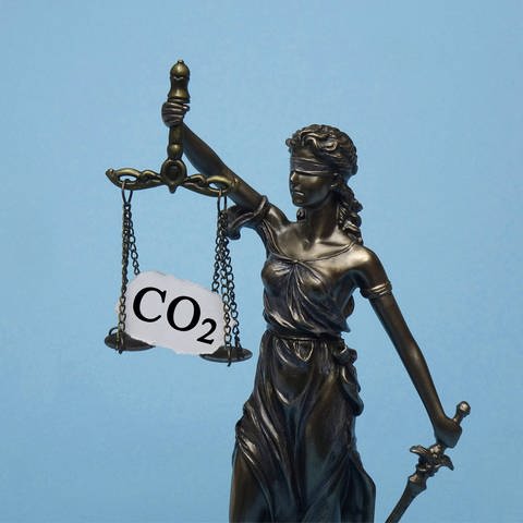 Justitia-Figur hebt eine Waage vor sich, auf der ein Schild mit Aufschrift "CO2" steht. (Foto: IMAGO, IMAGO / Steinach)
