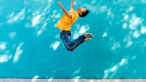Mann springt vor blauer Wand hoch in die Luft. Was ist Schwerkraft? (Foto: IMAGO, IMAGO / Westend61)