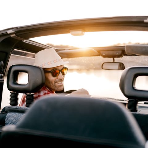 Mann mit Sonnenhut am Steuer eines Autos (Foto: IMAGO, Imago / Addictive Stock)