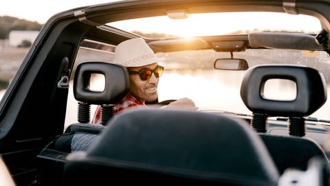 Mann mit Sonnenhut am Steuer eines Autos (Foto: IMAGO, Imago / Addictive Stock)