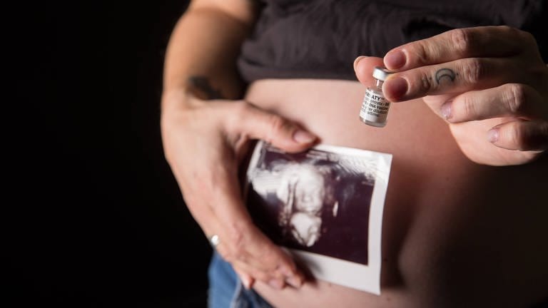 Frau hält Ultraschallbild und Impfampulle vor ihren schwangeren Bauch. (Foto: IMAGO, IMAGO / Fotostand)