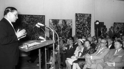 Werner Haftmann spricht während der Eröffnung der documenta 2 im Jahr 1959 in Kassel. Im Publikum vorn mit Brille der hessische Ministerpräsident Georg August Zinn mit Gattin und rechts daneben der Initiator der documenta, Arnold Bode (Foto: dpa Bildfunk, picture-alliance/ dpa | Eberth)