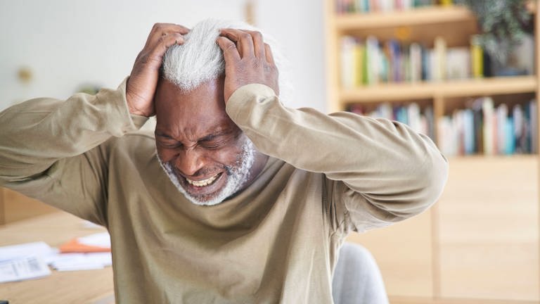 Älterer Mann mit schmerzverzerrtem Gesicht hält sich die Hände an den Kopf. (Foto: IMAGO, IMAGO / PhotoAlto)