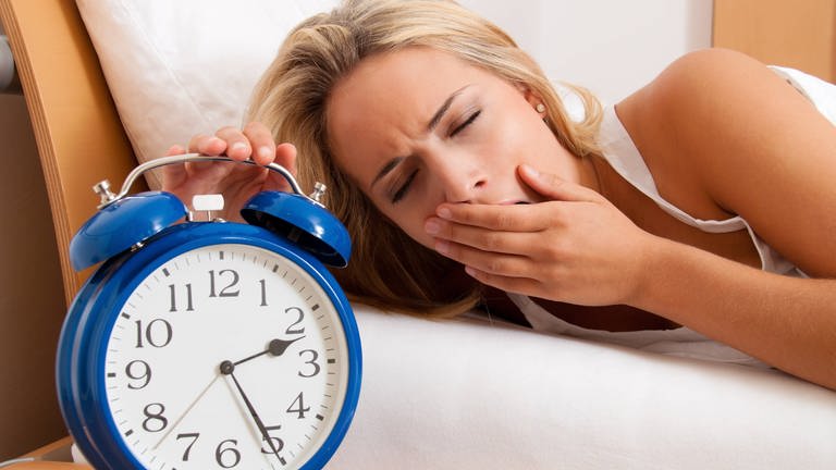  Blonde Frau liegt im Bett und kann nicht schlafen. Sie gähnt, ihr Wecker zeigt 2.25 Uhr in der Nacht (Foto: IMAGO, /McPHOTO)