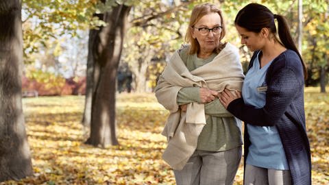 Das Bild zeigt eine ältere Frau mit einer Pflegerin im Park.  (Foto: IMAGO, Westend61)