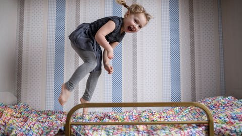 Das Bild zeigt ein Kind, das auf einem Hochbett springt und tobt. (Foto: IMAGO, Westend61)