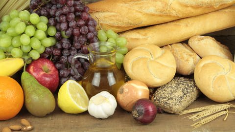 Verschiedenes Obst, Zwiebeln, Knoblauch, Saft und Brot liegen auf einem Tisch präsentiert. (Foto: IMAGO, IMAGO / agefotostock)