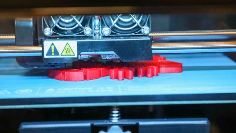 Ein 3D-Drucker druckt ein rotes Plastikelement schichtweise. (Foto: IMAGO, IMAGO / ZUMA Wire)
