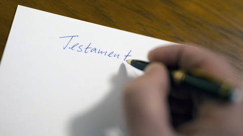 Das Bild zeigt eine Person, die auf ein Blatt Papier die Überschrift "Testament" geschrieben hat. (Foto: IMAGO, photothek)
