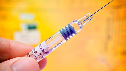Impfspritze vor einem Impfausweis (Foto: IMAGO, IMAGO / Christian Ohde)