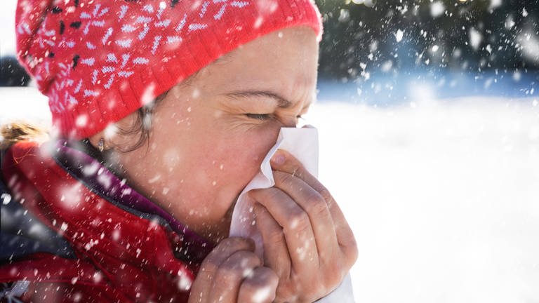Eine Frau putzt sich die Nase im Schnee. (Foto: IMAGO, IMAGO / Panthermedia)