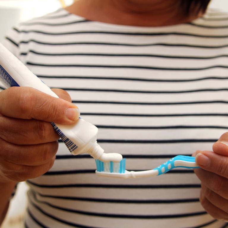 Eine Frau macht Zahnpasta auf ihre Zahnbürste. (Foto: IMAGO, CHROMORANGE)