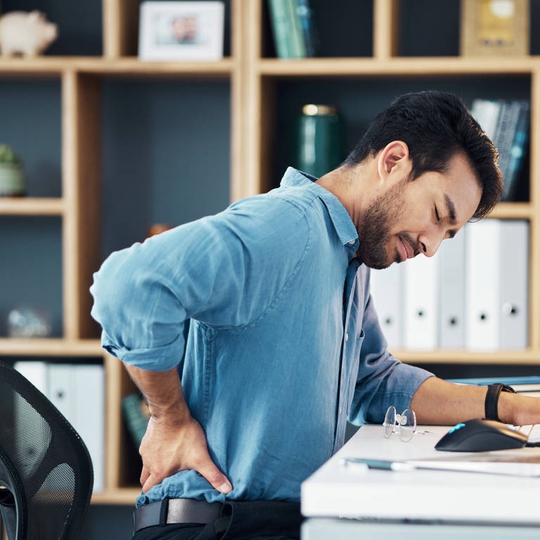 Mann sitzt am Schreibtisch mit Rückenschmerzen (Foto: IMAGO, Zoonar)