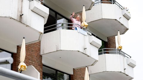Eine 96 jährige Bewohnerin des Altenheims Johannes-Höver-Haus steht auf dem Balkon ihres Zimmers und kommuniziert auf Distanz mit ihren Angehörigen. (Foto: IMAGO, imago images / Norbert Schmidt)