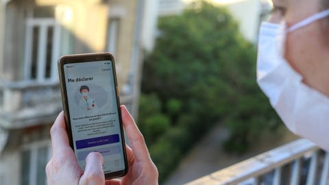 Person mit Maske hält Smartphone mit der französischen App "StopCovid" in den Händen (Foto: IMAGO, imago images / Hans Lucas)