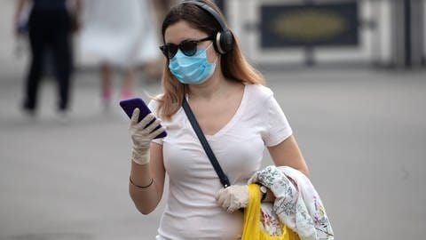 Frau mit Mund-Nasen-Schutz, Handschuhen und Smartphone (Foto: IMAGO, imago images / ITAR-TASS)