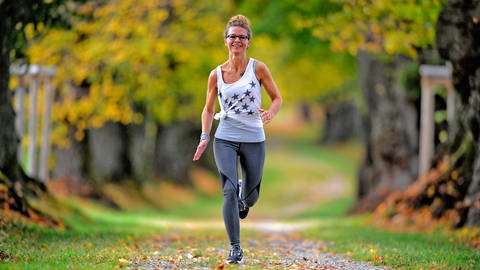 Frau joggt durch sonnigen Herbst-Wald (Foto: IMAGO, imago / MiS)