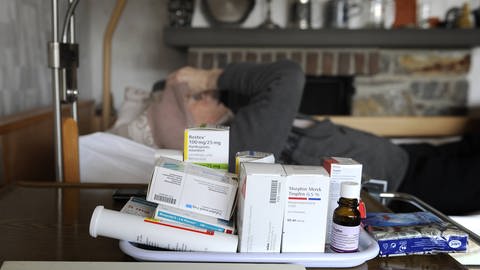 Schwerstkranker Mann wird zu Hause palliativ behandelt, vor seinem Pflegebett steht ein ganzes Arsenal von schmerzlindernden Medikamenten (Foto: IMAGO, imago images/Sven Simon)