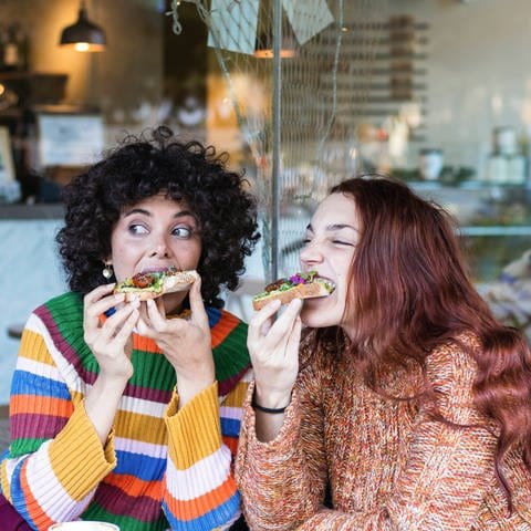 Zwei Frauen beißen beim Frühstück herzhaft in belegte Brote.