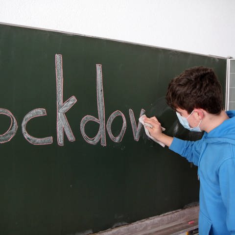Schüler wischt "Lockdown"-Aufschrift von Tafel (Foto: IMAGO, IMAGO / Eibner)