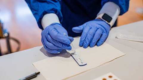 Mitarbeiter einer Schnellteststation tropft Probe mit Gummihandschuhen auf Schnelltest. (Foto: IMAGO, IMAGO / KS-Images.de)