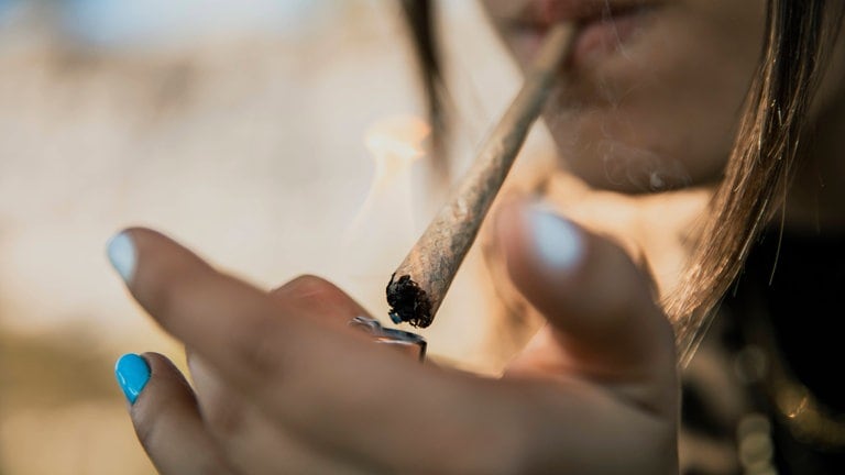 Junge Frau zündet sich eine Zigarette mit Marihuana an.