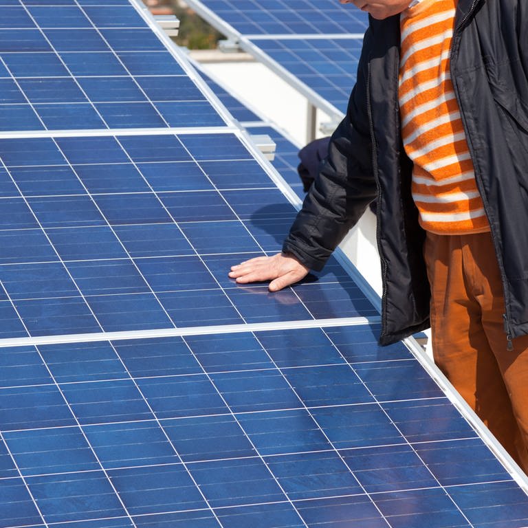Ein Mann steht neben einem Solarmodul. (Foto: IMAGO, IMAGO / Shotshop)