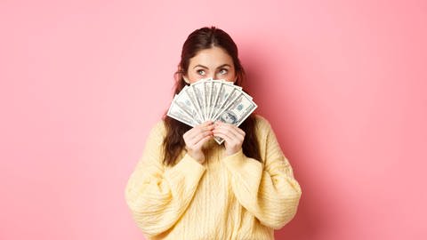 Junge Frau mit vielen Geldscheinen: Laut Studien zum Glück ist finanzielle Sicherheit eng verbunden mit emotionalem Wohlbefinden (Foto: IMAGO, IMAGO / YAY Images)