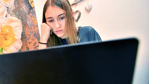 Mädchen sitzt vor einem PC mit einer Hand an der Backe gestützt (Foto: IMAGO, /Jan Huebner)