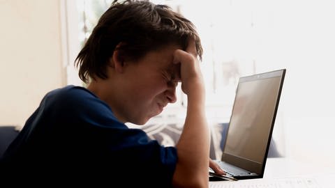 Junge sitzt angestrengt vor dem Laptop und hält die Hand vor die Stirn (Foto: IMAGO, CHROMORANGE)