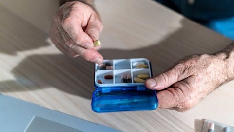 Ein Mann nimmt Medikamente aus einer Medikamentendose. (Foto: IMAGO, IMAGO / Westend61)