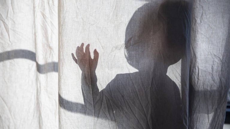 Schatten eines kleinen Kindes, das hinter einem Vorhang steht und die Hand hebt.