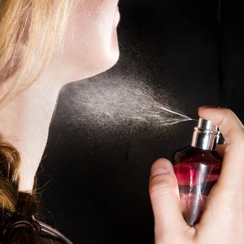 Parfüm kann Allergien auslösen - Eine Frau sprüht sich Parfum auf den Hals