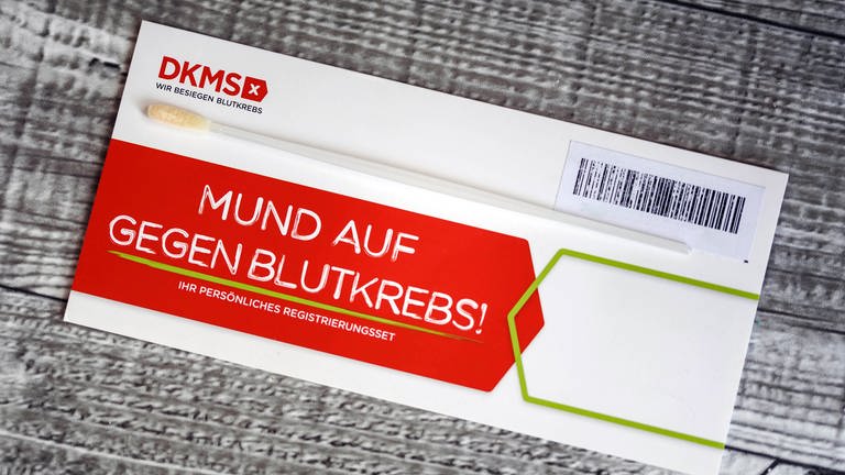 DKMS-Logo auf einem Umschlag mit dem Test-Stäbchen für die Typisierung potentieller Spender mit Zellen der Mundschleimhaut.  (Foto: IMAGO, /Future Image)