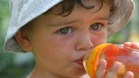 Kleines Kind mit Sonnenhut trinkt aus einer Flasche